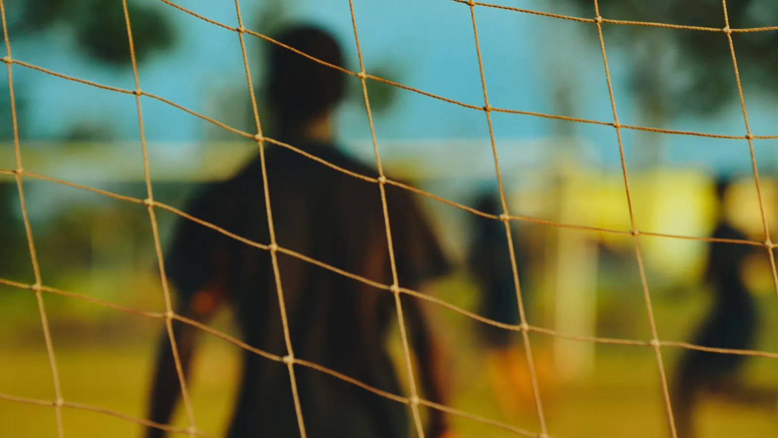Joueur flou vu de dos à travers les mailles d'un filet de but de soccer