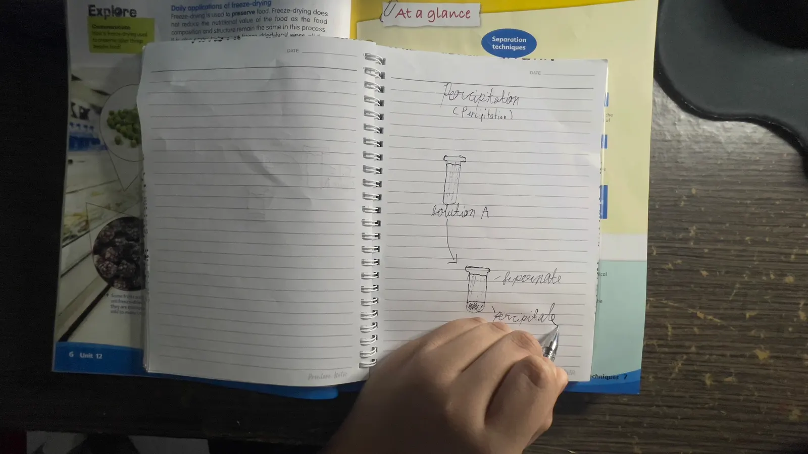 Cahier à spirale ouvert avec des notes manuscrites et une main qui tient un stylo