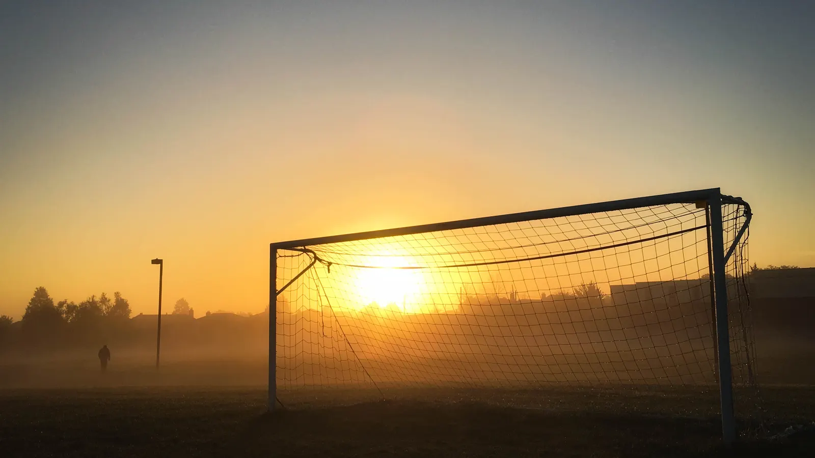 But de soccer et filet en silhouette devant un soleil bas et orangé sur un terrain de parc dans la brume